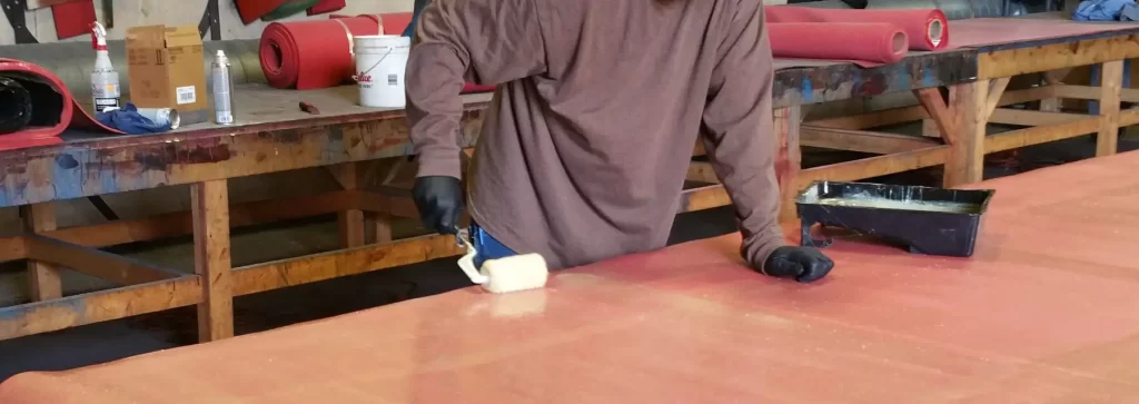 Photo of glue being applied to a red rubber sheet, a crucial step in the manufacturing process of wear-resistant rubber linings. The glue quality and thickness affect bonding effectiveness.